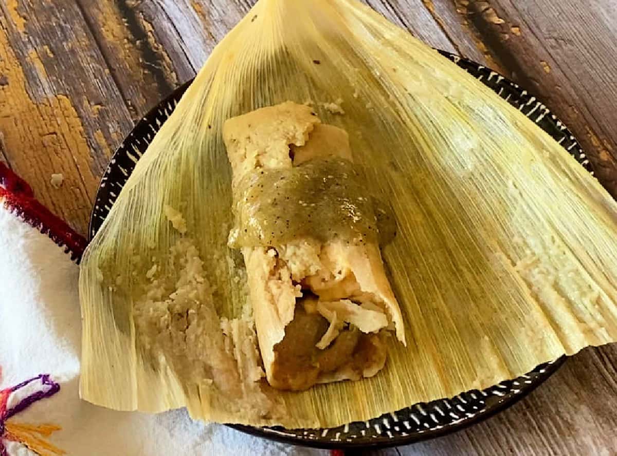 An instant pot chicken tamal sitting on top of a corn husk and topped with salsa verde.