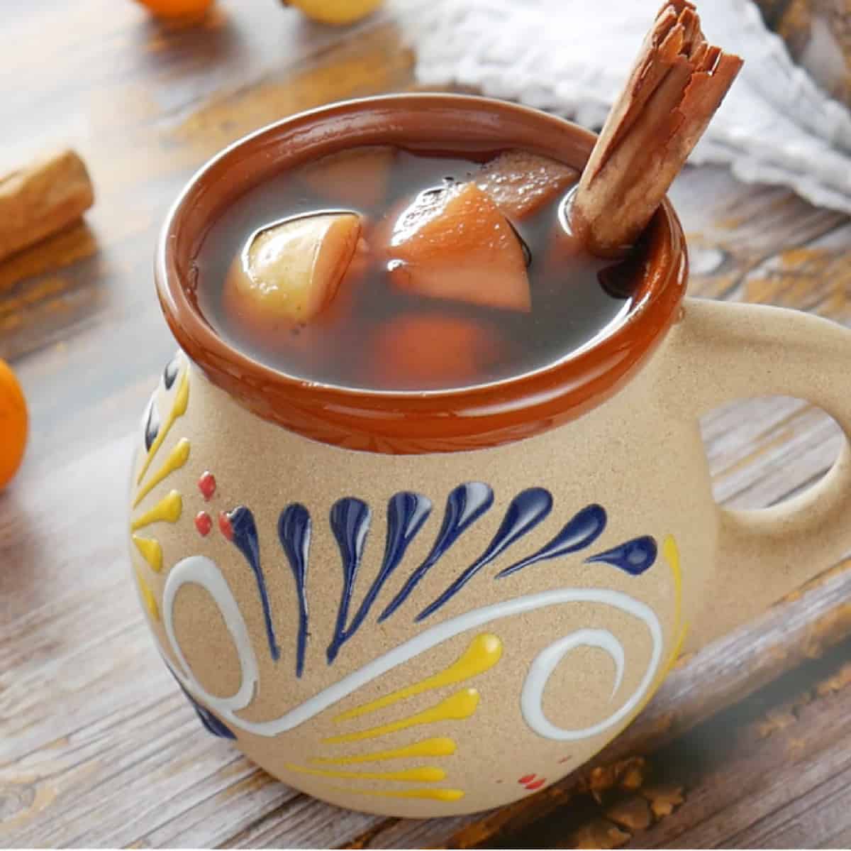 Ponche Navideño (Mexican Christmas Punch) served in a decorative clay mug with a cinnamon stick.