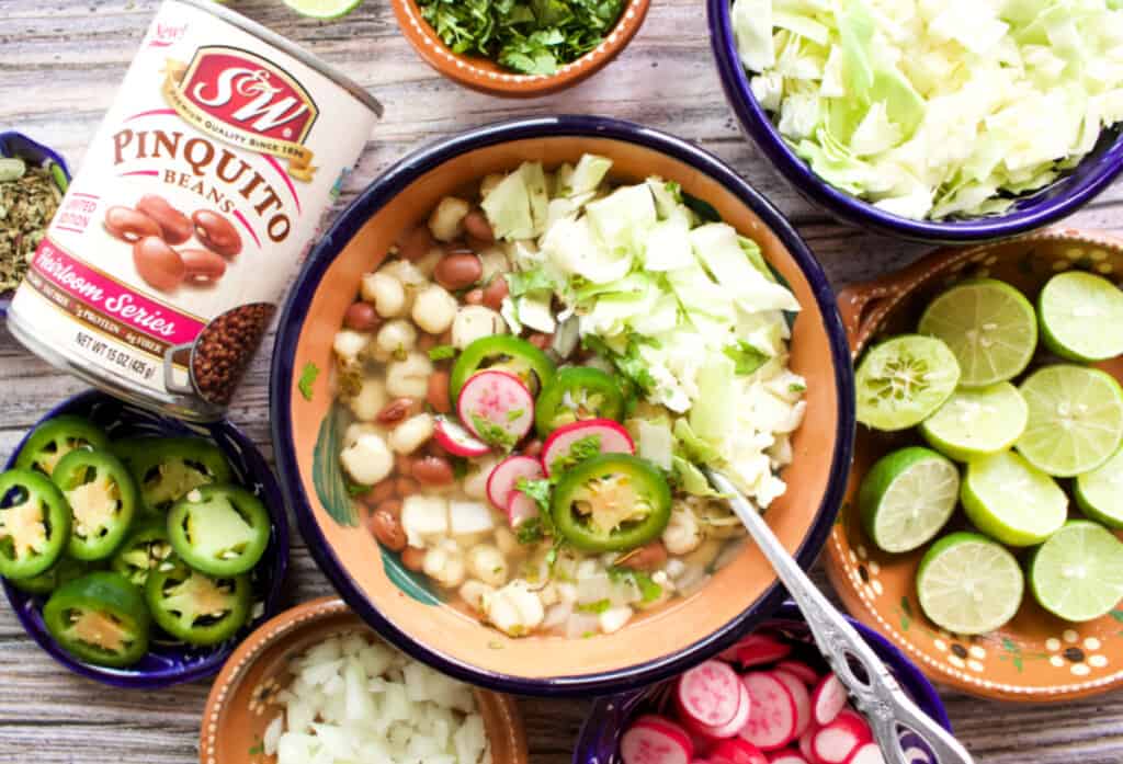 A bowl of pozole de frijol topped with cabbage, jalapeno slices, and radishes.