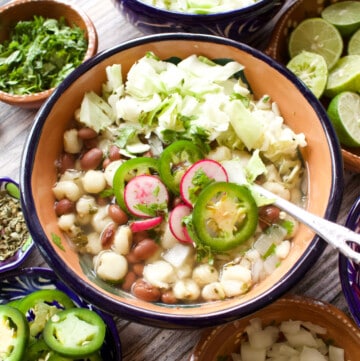 A bowl of bean pozole topped with cabbage, jalapeno slices, and radishes.