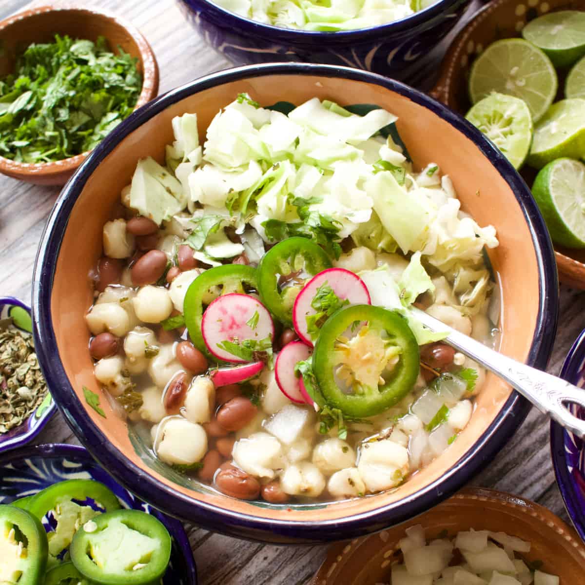 A bowl of bean pozole topped with cabbage, jalapeno slices, and radishes.