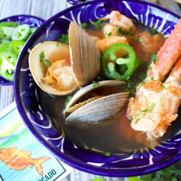 Siete Mares Soup served in a decorative blue bowl surrounded by toppings and a Mexican loteria card.