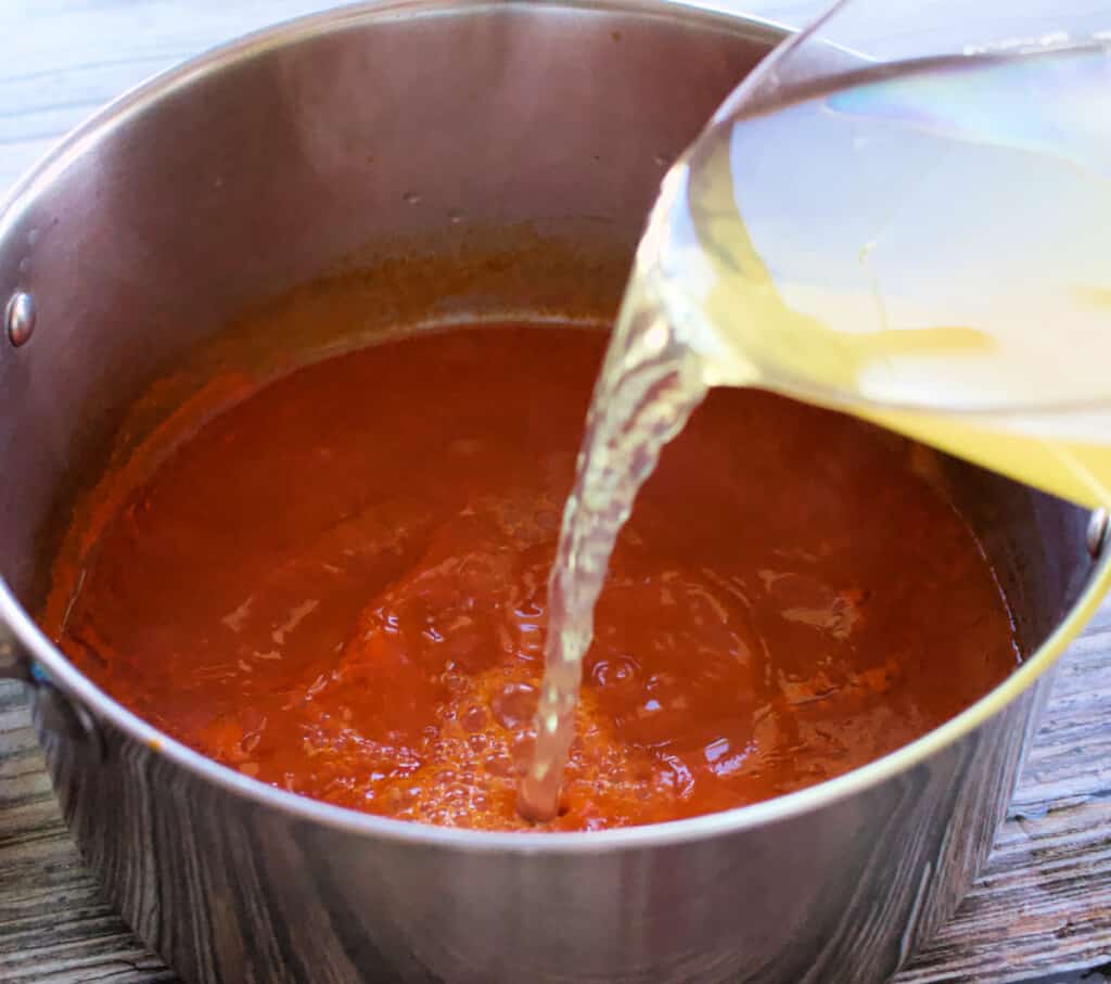 Shrimp broth pouring into the stock pot with guajillo tomato sauce.