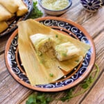 Green Pork Tamales on a decorative plate served next to a bowl of salsa verde.
