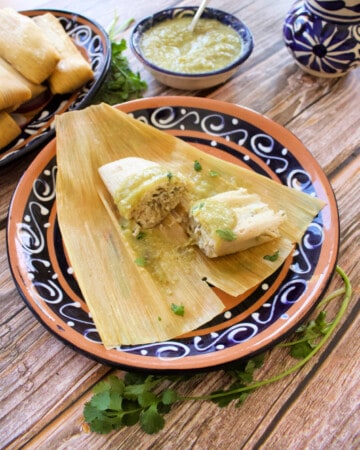 Green Pork Tamales on a decorative plate served next to a bowl of salsa verde.