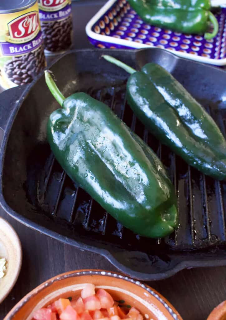 A picture of two poblano peppers roasting on a grill pan.