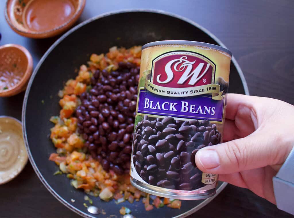 A hand holding a can of S&W Black Beans.