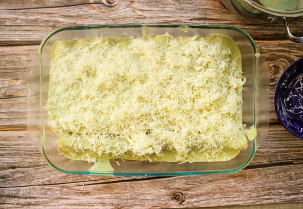 Chicken Enchiladas Suizas in a glass baking dish topped with cheese waiting to be put in the oven.