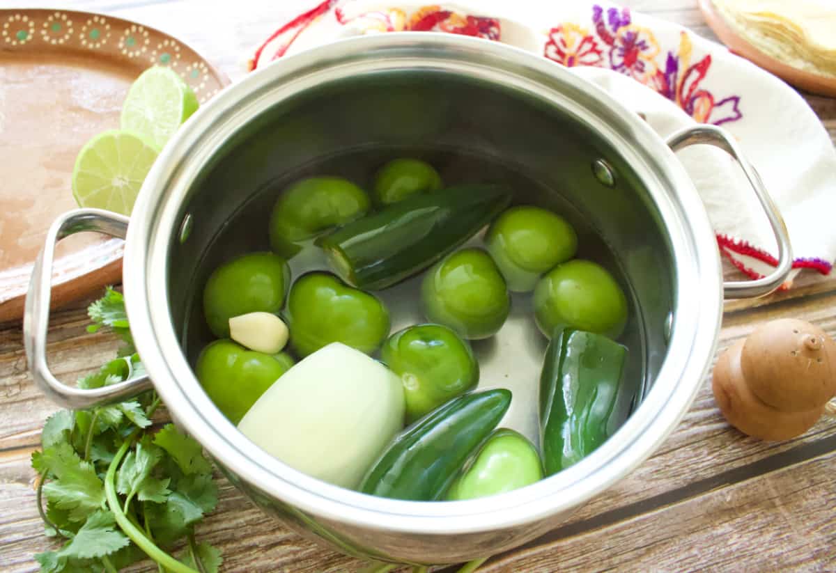 A pot with uncooked tomatillos and other ingredients need to make the creamy green salsa.