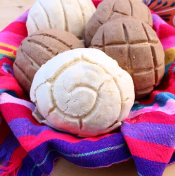 A pile of Mexican conchas sitting on a decorative and colorful basket.