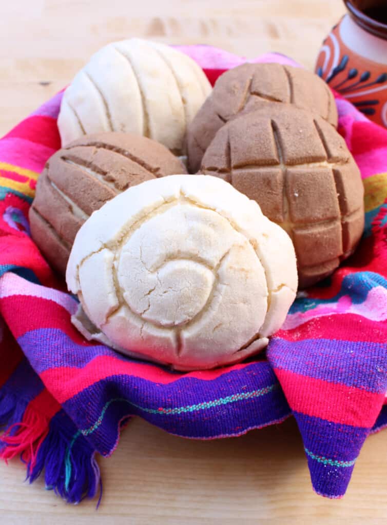 A pile of Mexican conchas sitting on a decorative and colorful basket.