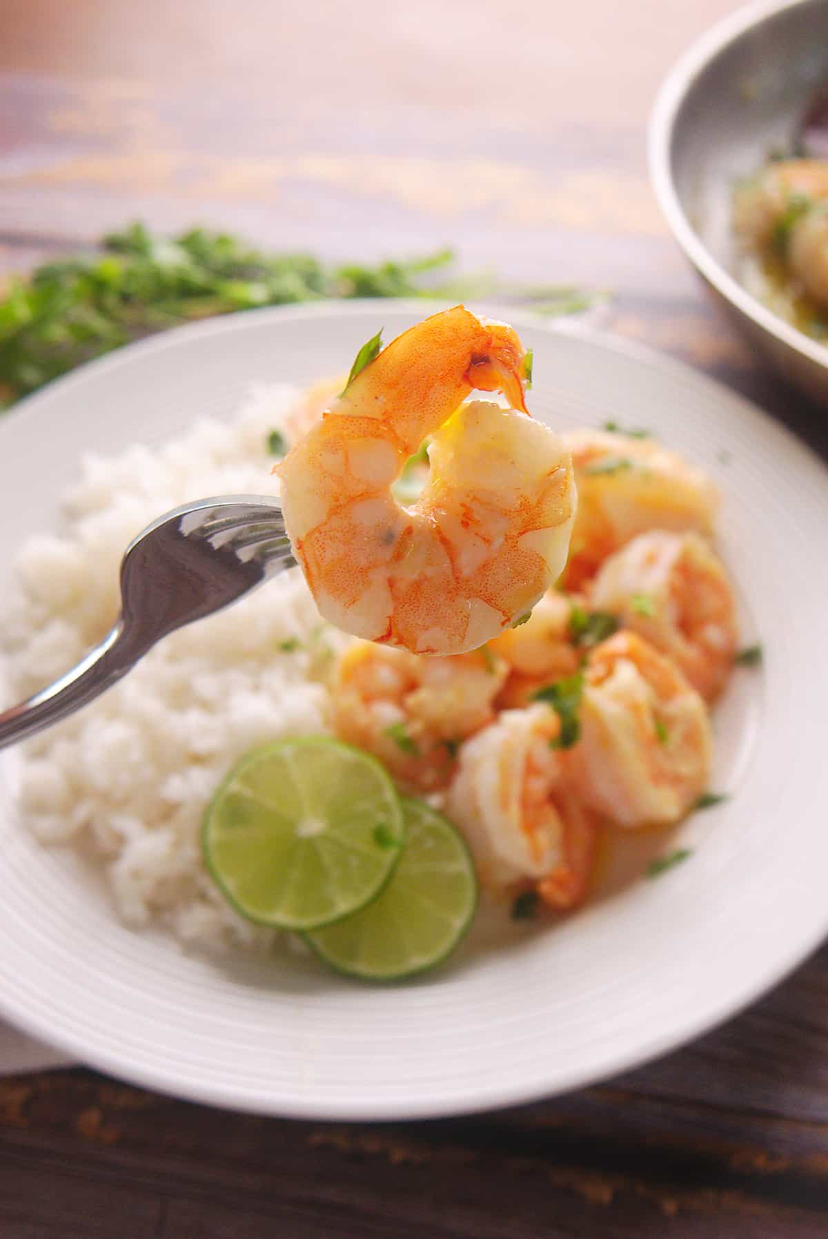 A fork holding a shrimp above a plate of Camarones al Mojo de Ajo. 