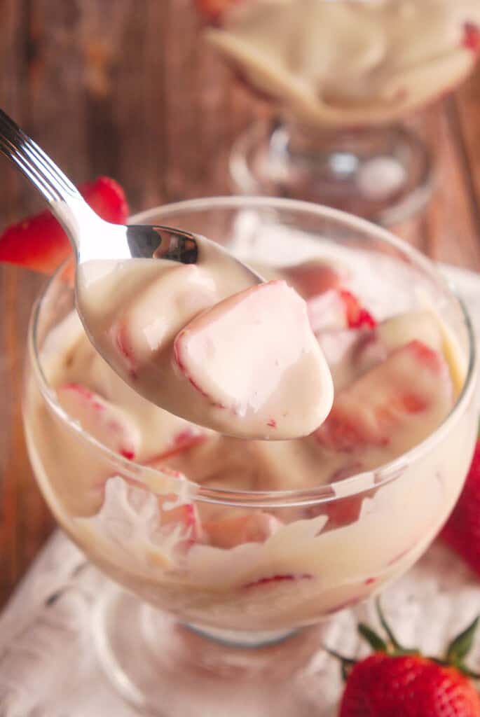 A spoon of sliced strawberries with cream