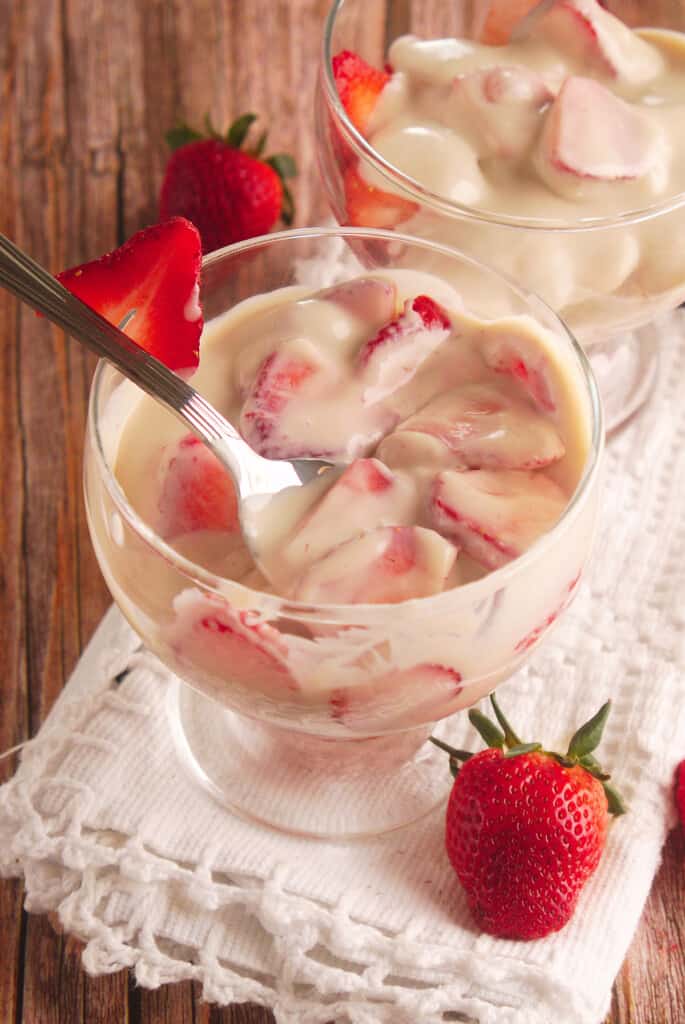 Fresas con Crema served in a glass cup with a spoon holding strawberries.