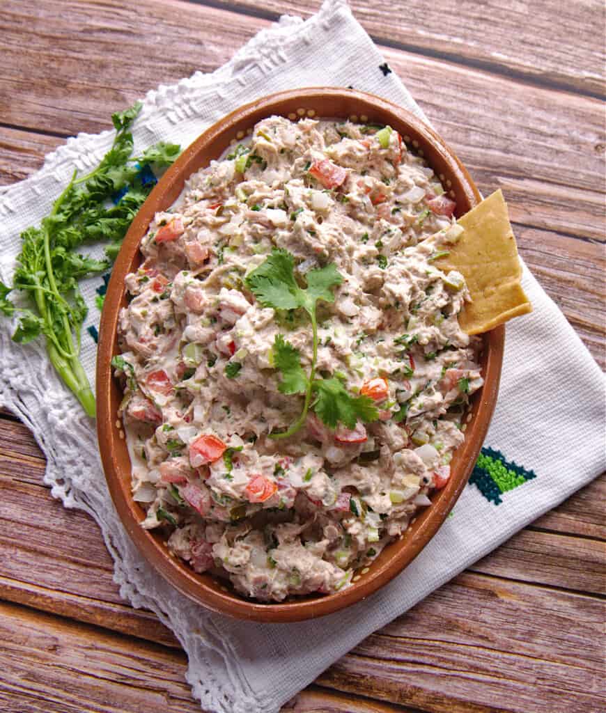 Ensalada de Atún served in a large clay bowl and decorated with a cilantro leaf and a single tortilla chip.