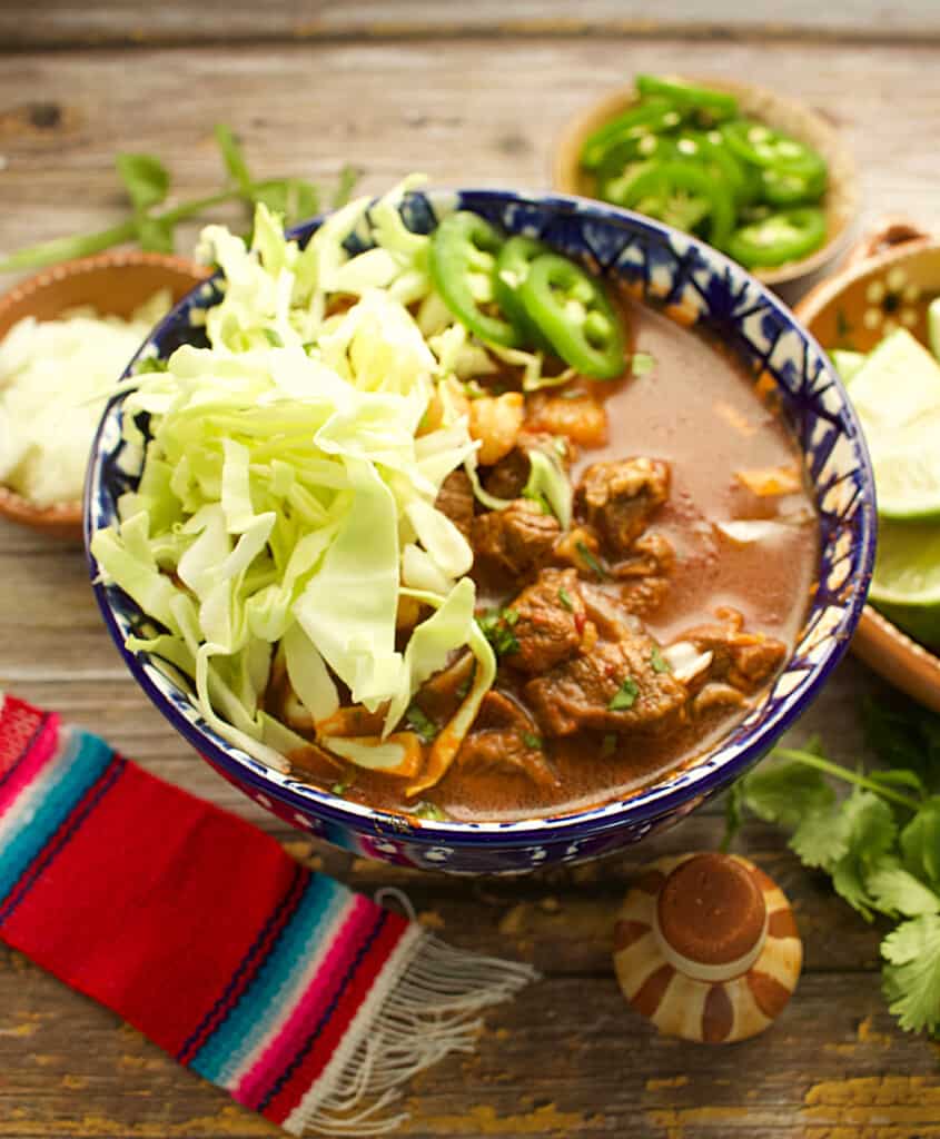 Red Beef Pozole served in a decorative blue bowl and topped with cabbage.