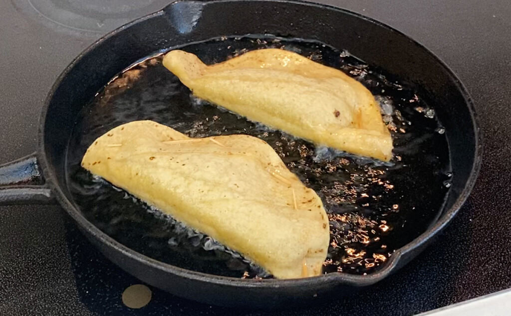 Tacos frying a cast iron skillet.