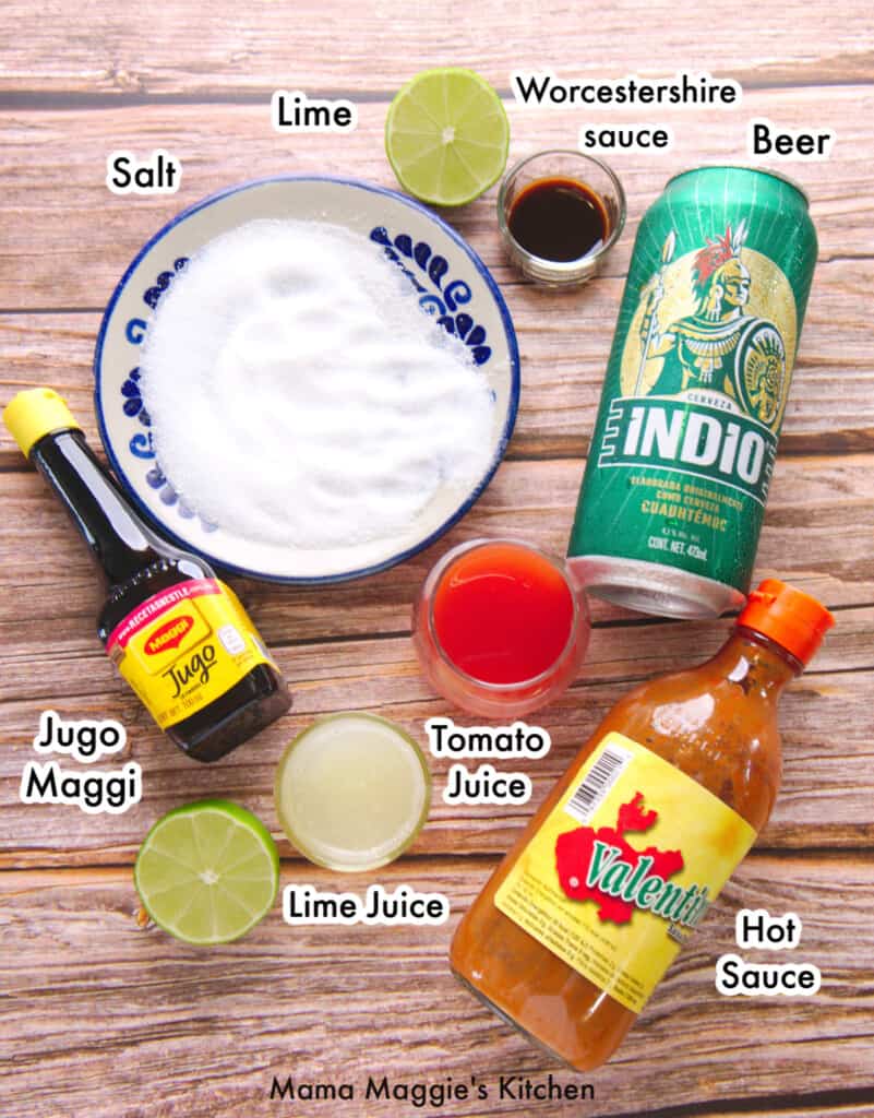 The ingredients needed to make a michelada labeled and sitting on a wooden surface.