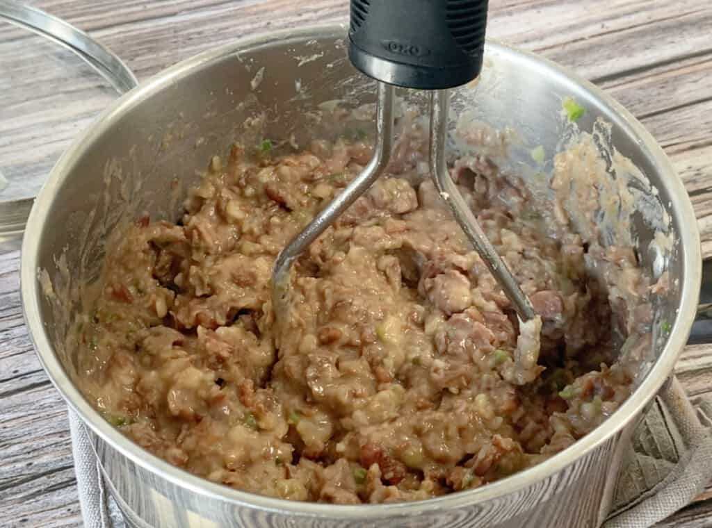 A potato masher inside a pot with pinto beans.