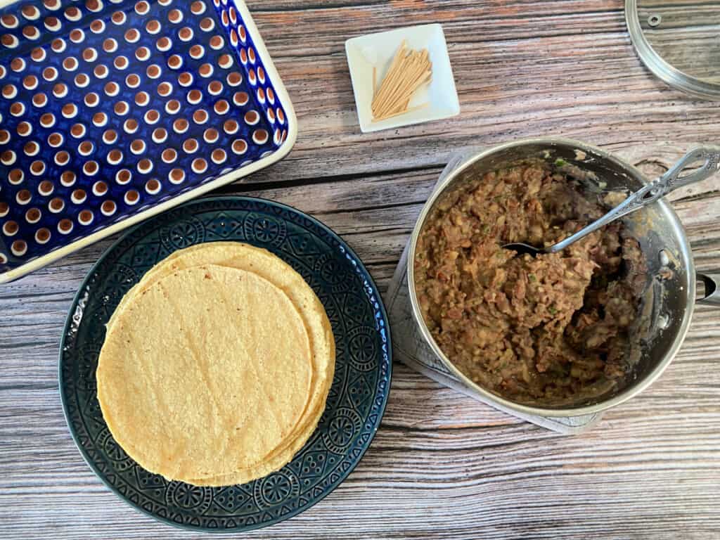 A pot with refried beans next to a plate of corn tortillas.