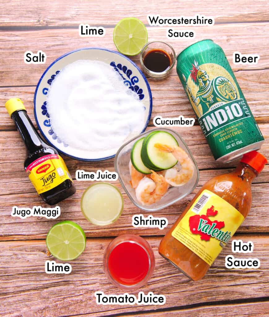 The ingredients needed to make Shrimp Micheladas labeled and sitting on a wooden surface.