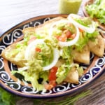 A plate of Tacos Dorados de Frijoles topped with lettuce, tomatoes, and more.