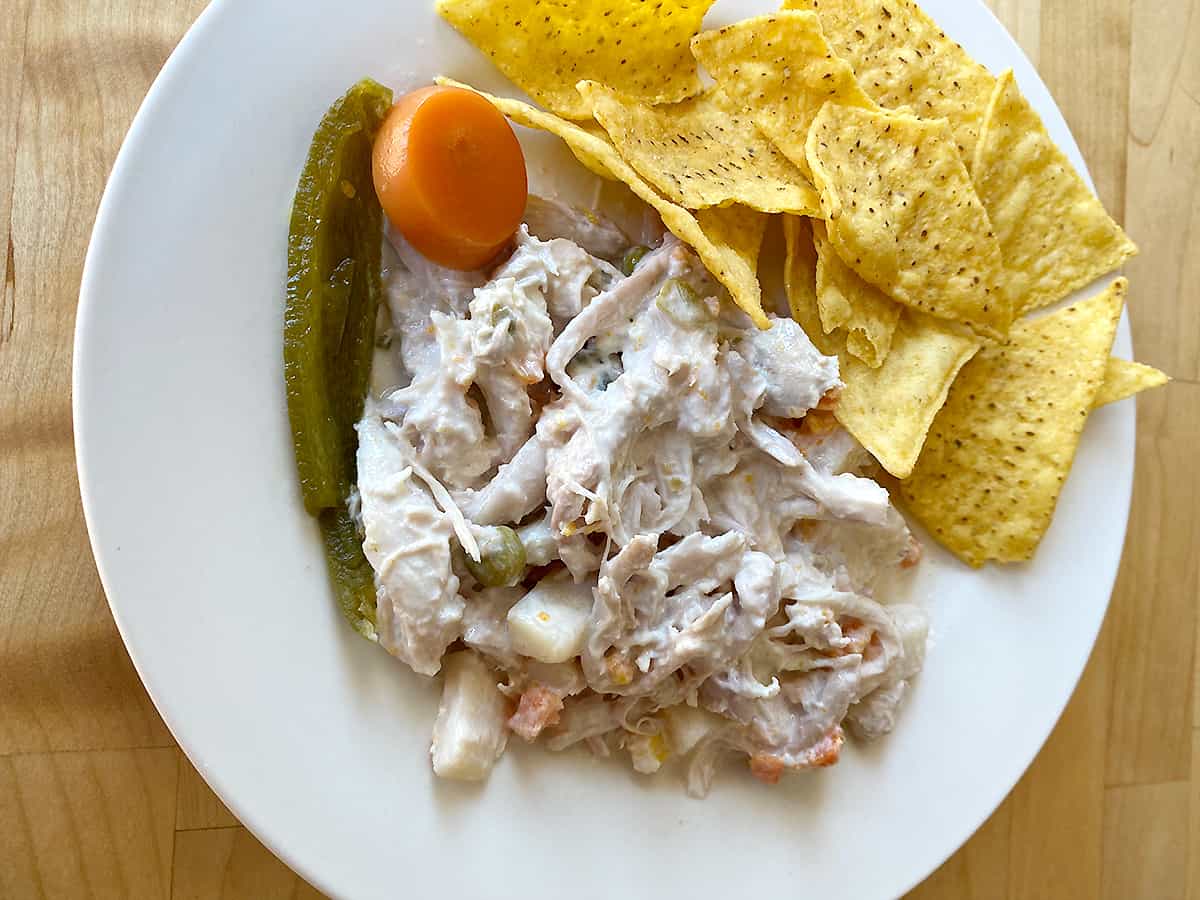 Ensalada de pollo, or chicken salad, served on a plate with tortilla chips and jalapeño