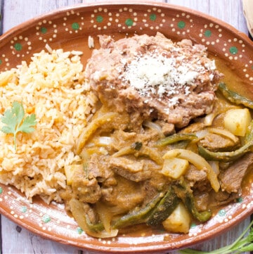 Bistec Ranchero served on a decorative Mexican clay plate next to beans and rice.