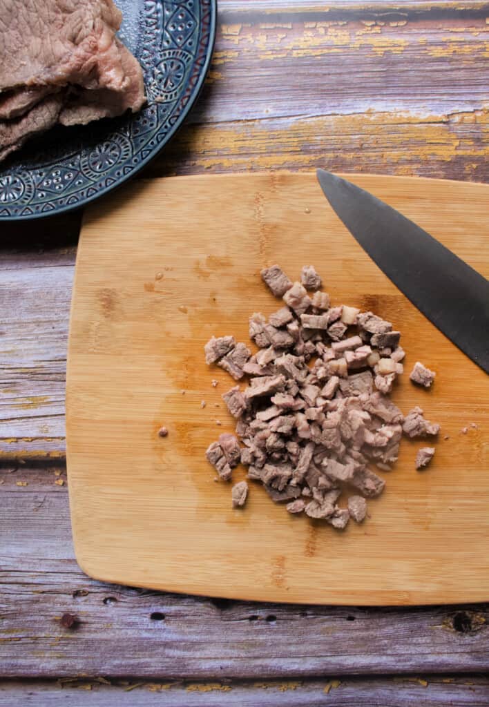 Diced beef on a wooden surface next to a chef knife.