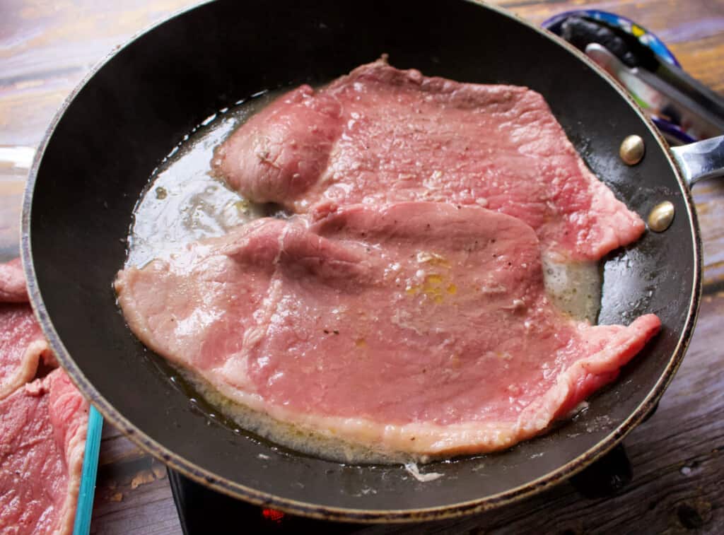 Two thin slices of beef cooking in a pan.