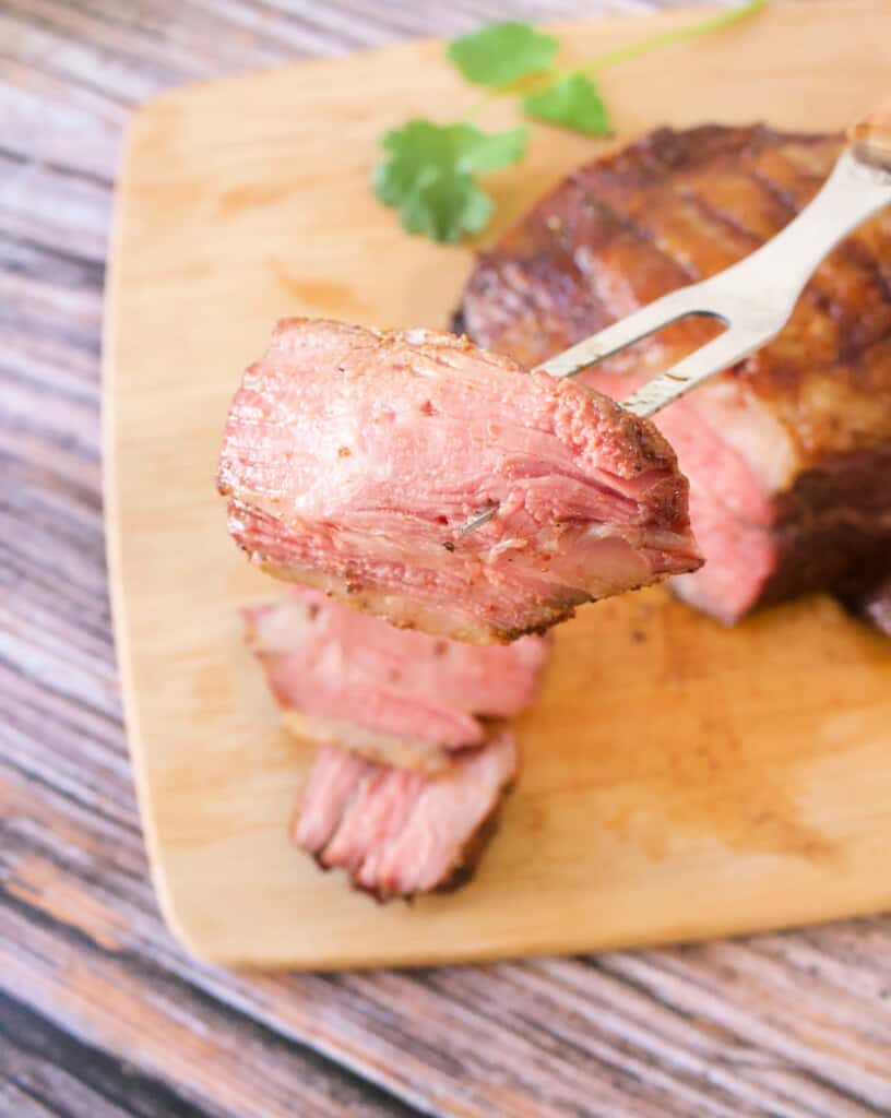 A fork holding a slice of grilled tri-tip steak with Mexican dry rub.