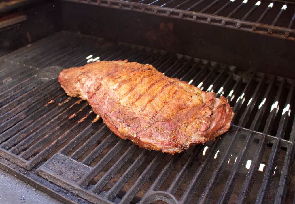 A tri-tip cooking on a black grill.