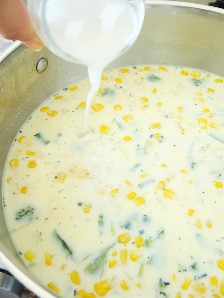 A hand pouring a corn starch and water mixture into a large stock pot.