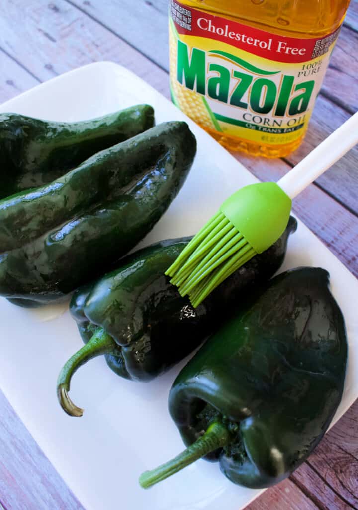 A brush brushing oil on a poblano pepper.