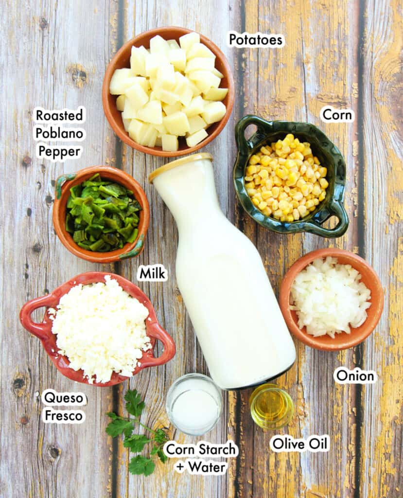 The ingredients needed to make Mexican potato and cheese soup labeled and laid out on a wooden surface.