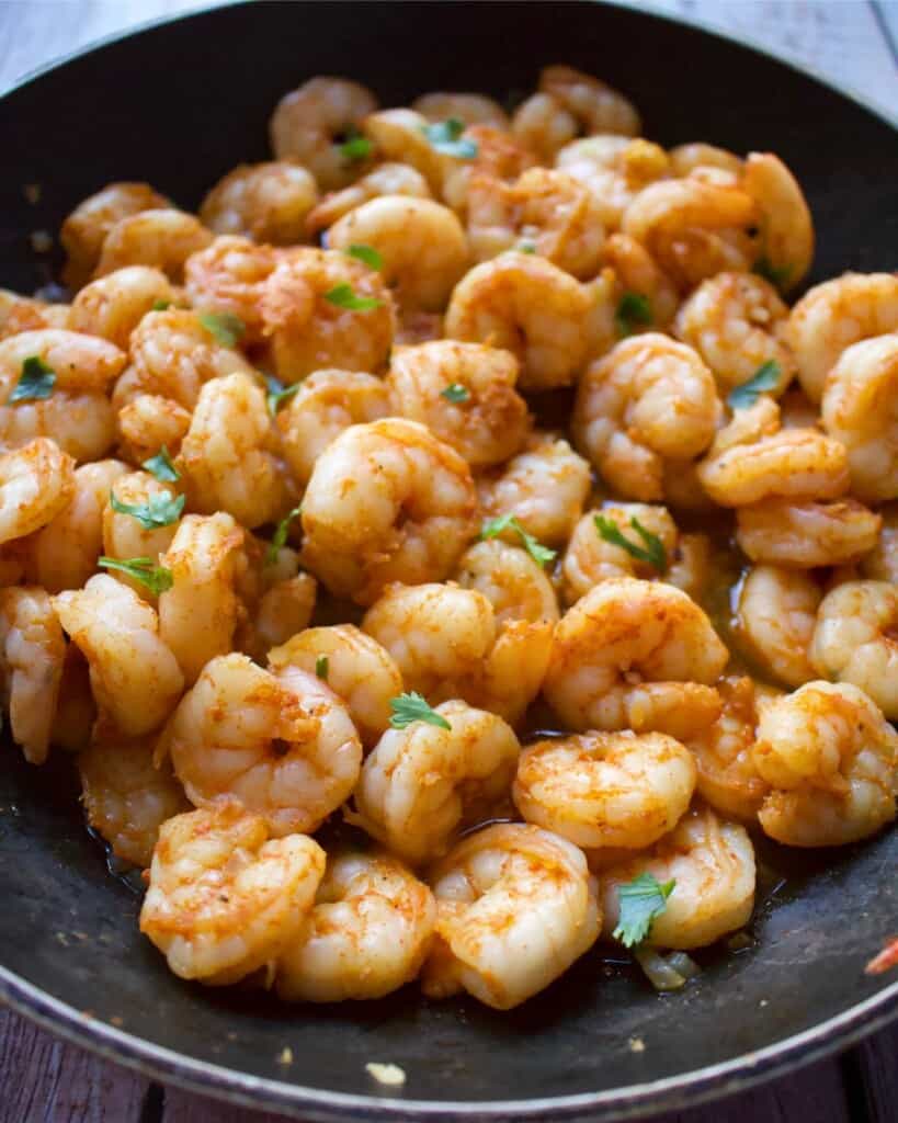 Cooked shrimp topped with cilantro in a black skillet.