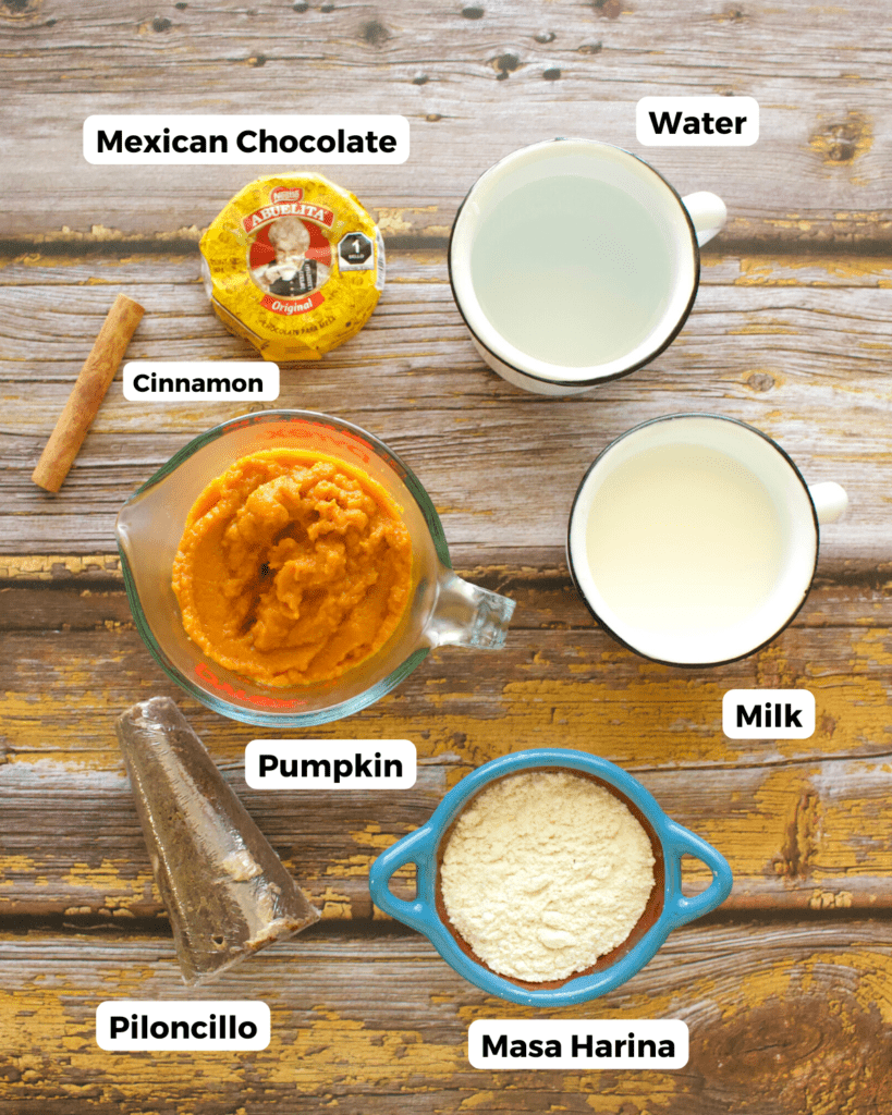 The ingredients needed to make pumpkin champurrado laid out and labeled on a wooden surface.