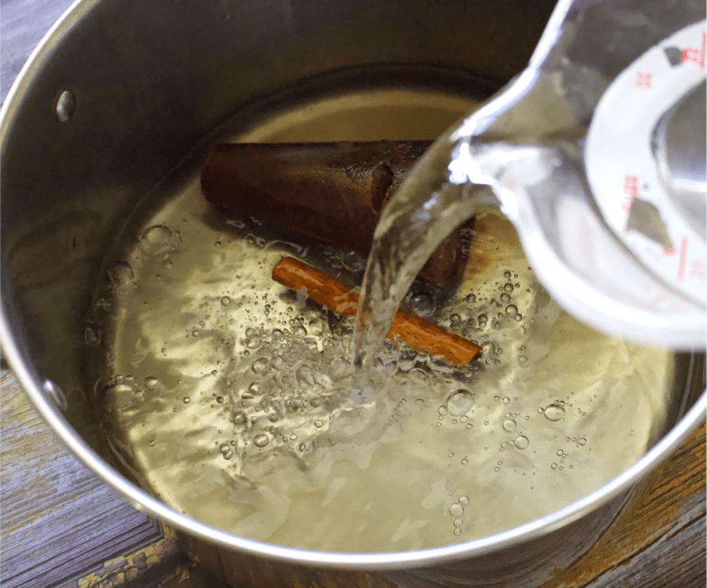 Water pouring into a stock pot with a piloncillo cone and a cinnamon stick.