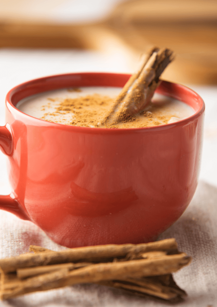 A red cup of Atole de Avena with a cinnamon stick.