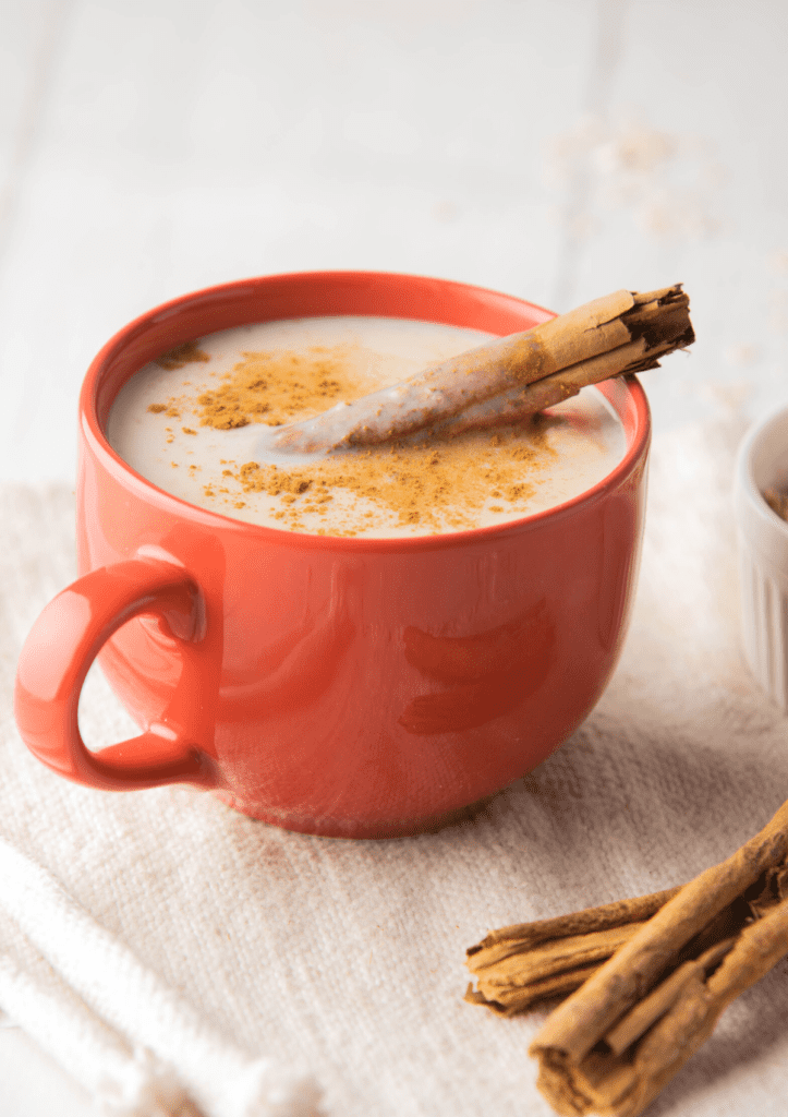 A red cup of Atole de Avena with a cinnamon stick sitting on a white napkin.