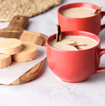A red cup of atole de mazapan served with a cinnamon stick.