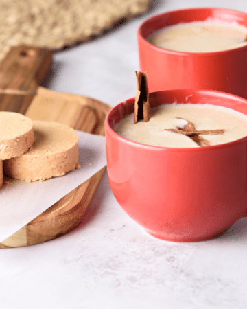 A red cup of atole de mazapan served with a cinnamon stick.