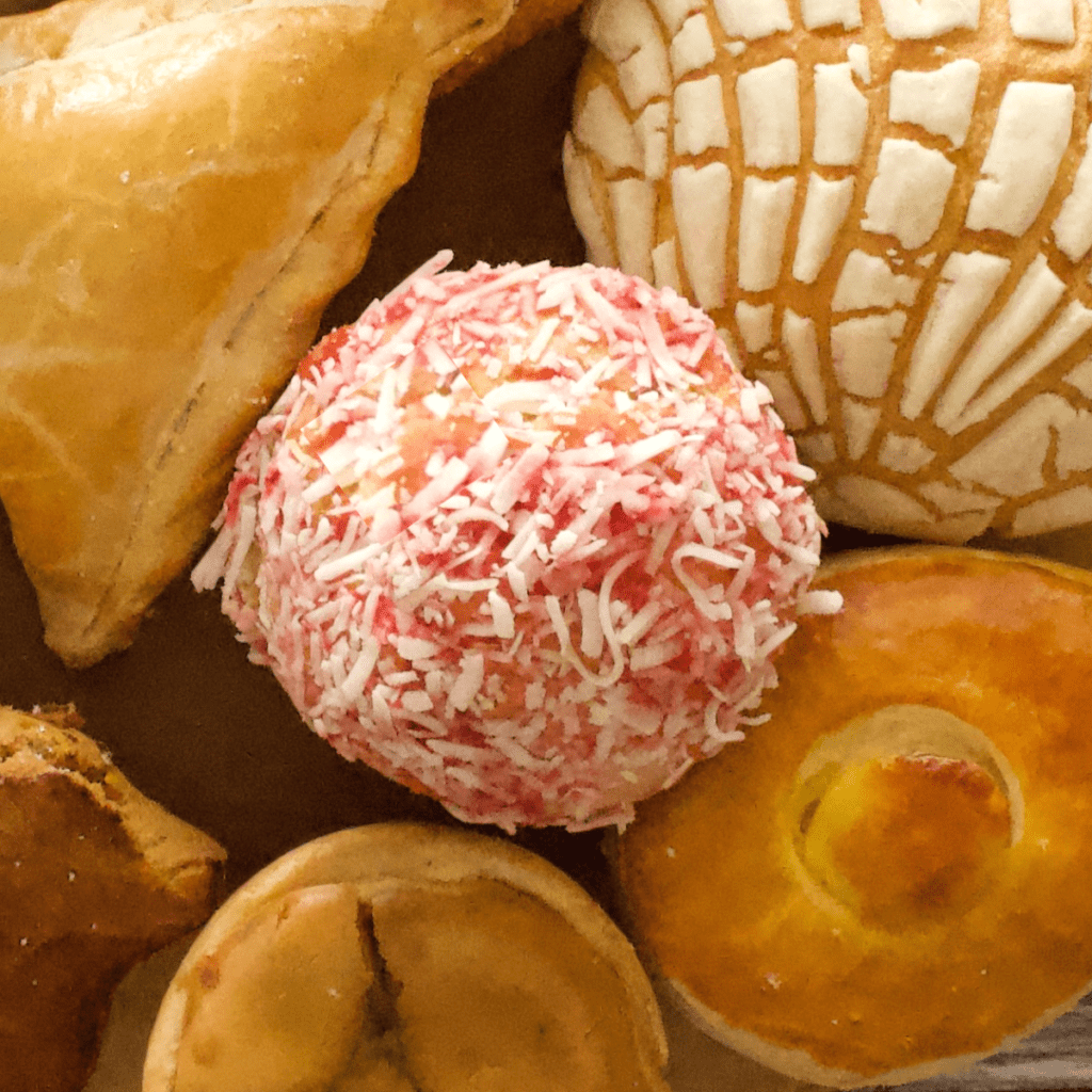 A besos pan dulce sitting next to other Mexican sweet breads and topped with shredded coconut.