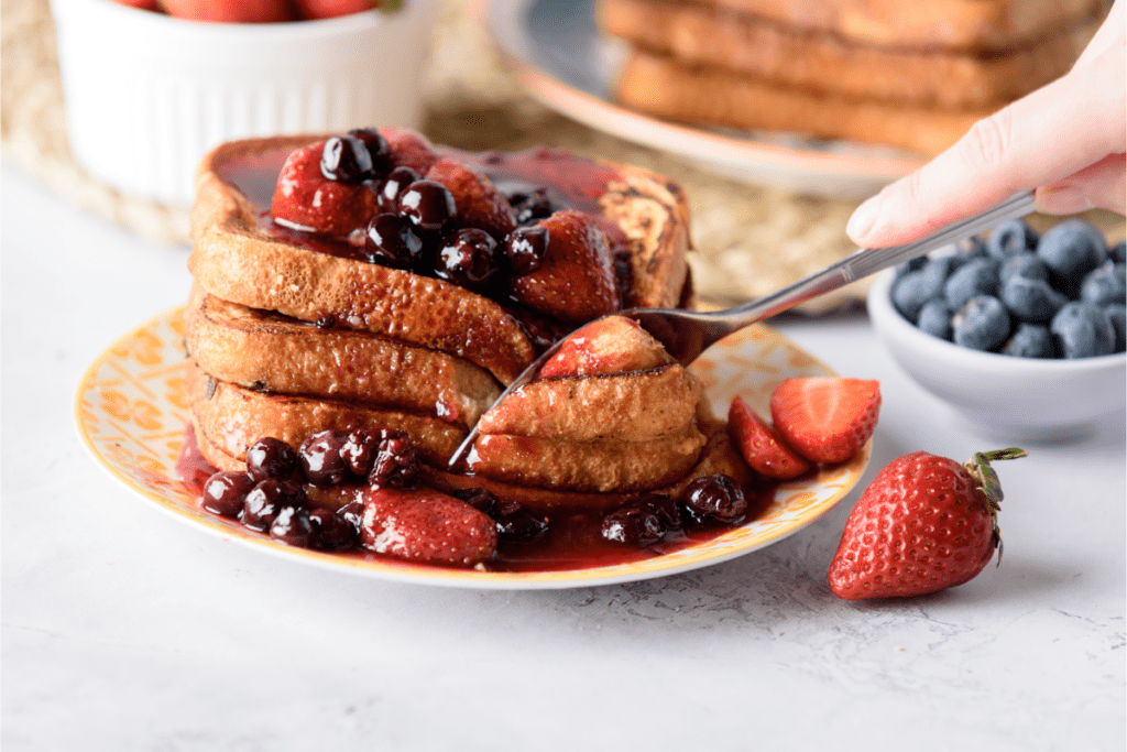 A fork cutting into a stack of pan frances surrounded by berries.