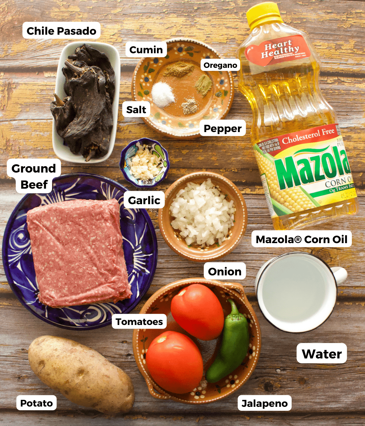 The ingredients needed to make Mexican picadillo labeled on a wooden surface.