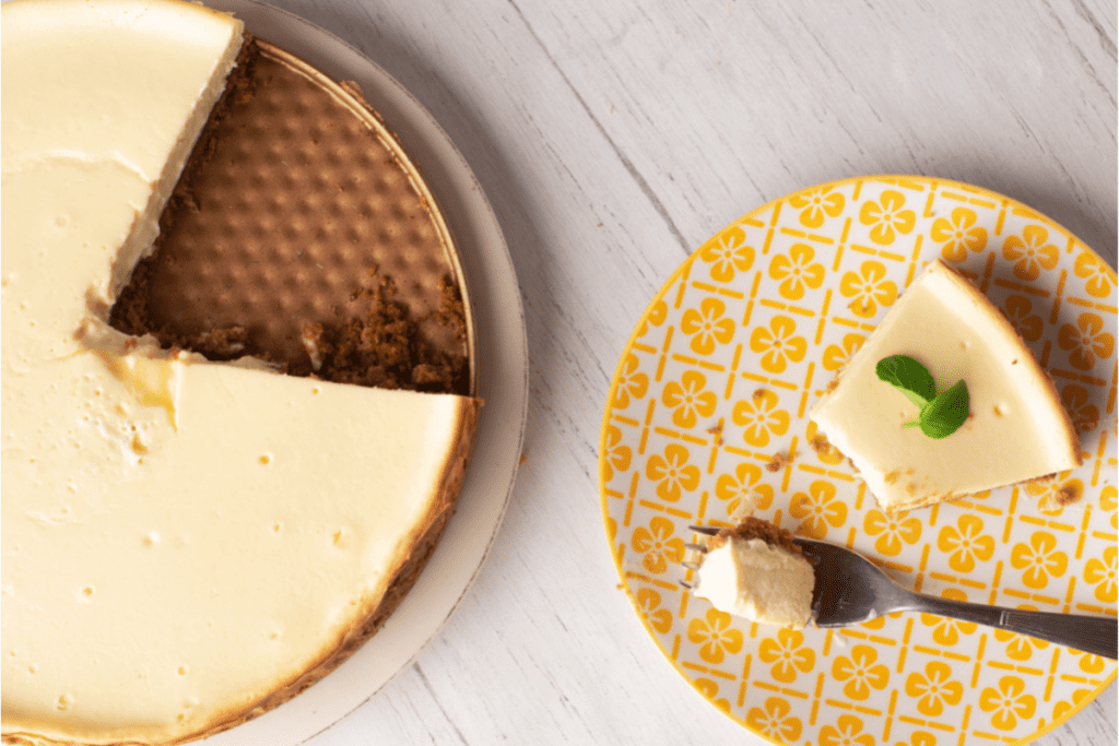 A slice of Pay de Queso served on a yellow cake next to the cut in pie.