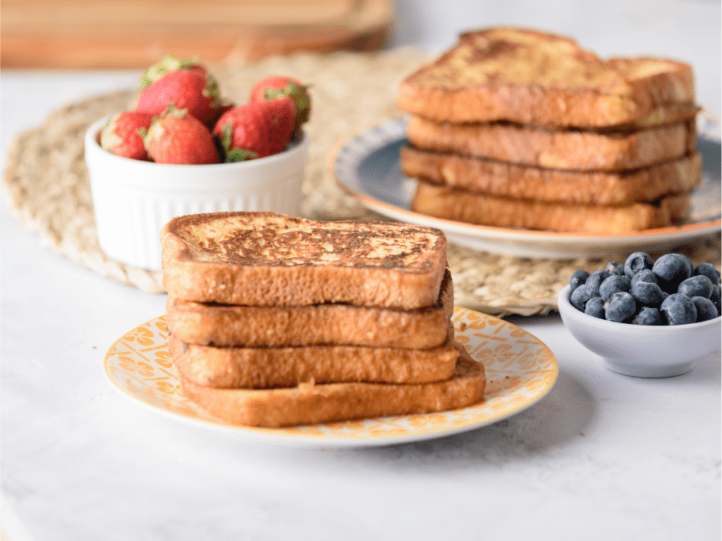 A stack of french toast on a yellow plate surrounded by berries.