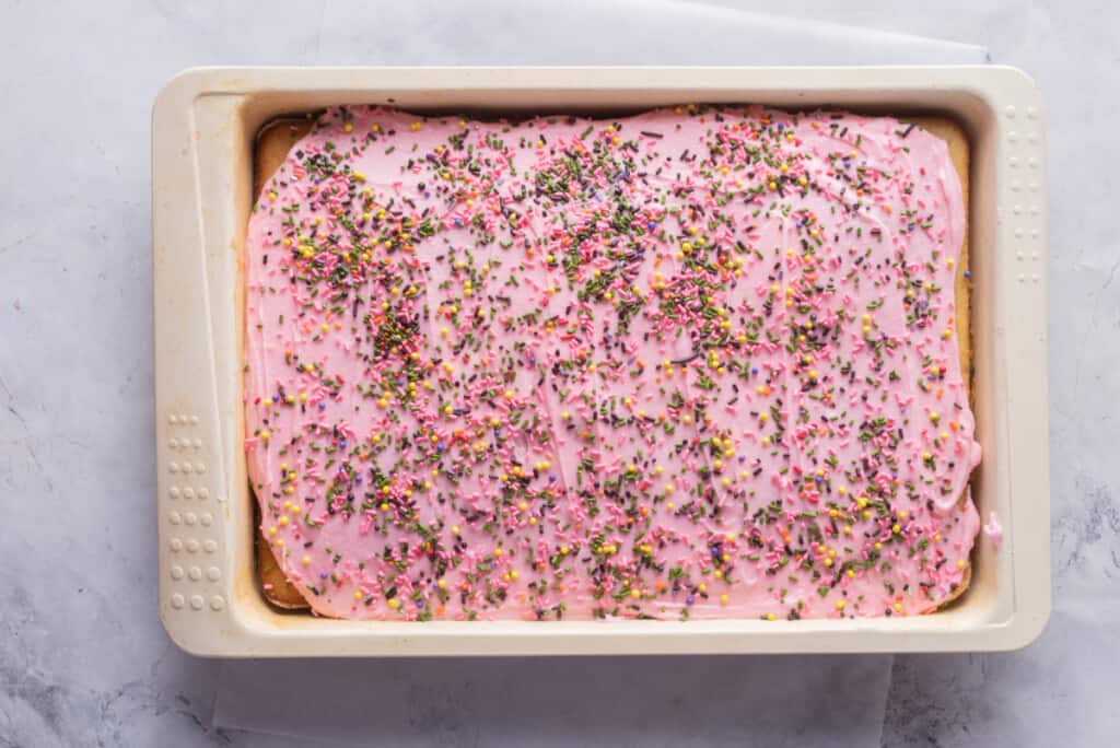 Freshly baked cortadillo cake in a baking pan topped with pink frosting and sprinkles.