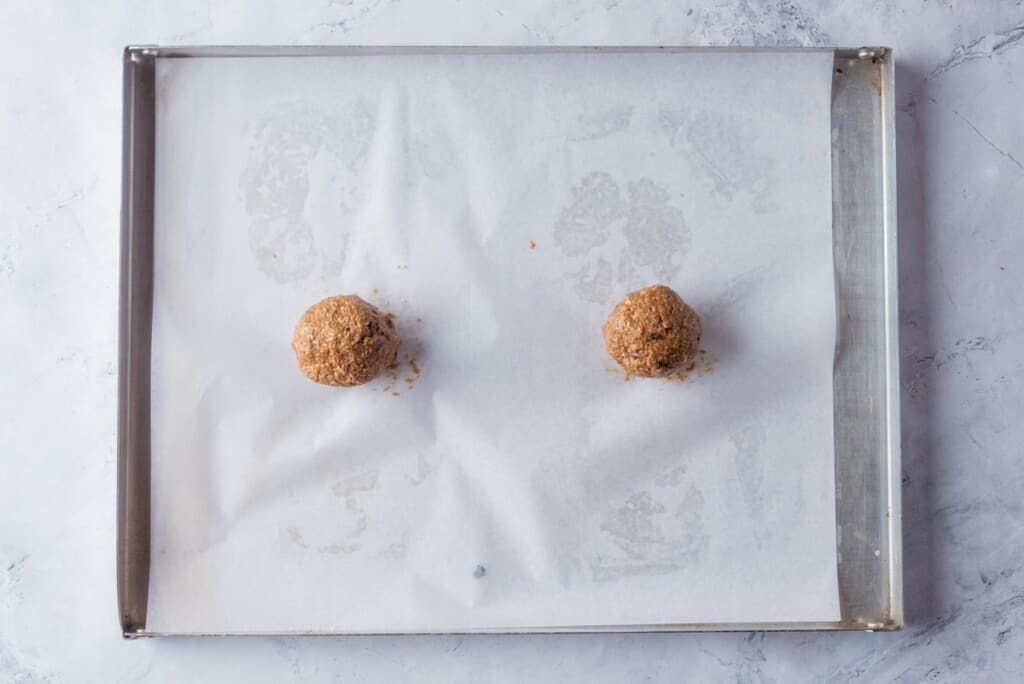 Two balls of oatmeal cookie dough balls on a baking sheet ready to bake.