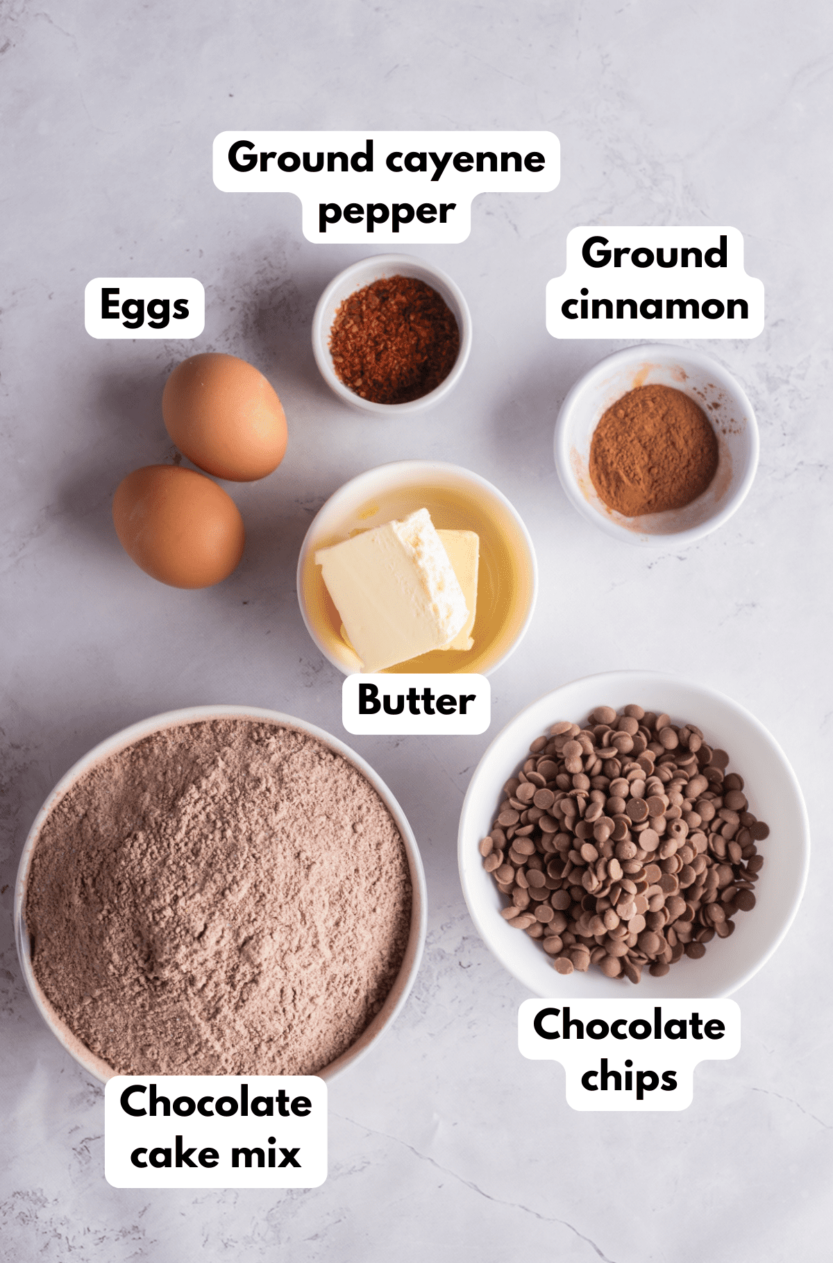 The ingredients needed to make Mexican spiced chocolate cookies labeled and sitting on a white marble surface.